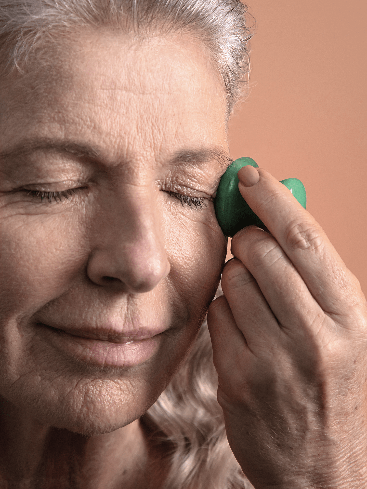 Woman using jade De-Puffing Eye Massage Tool along eyes to decrease puffiness