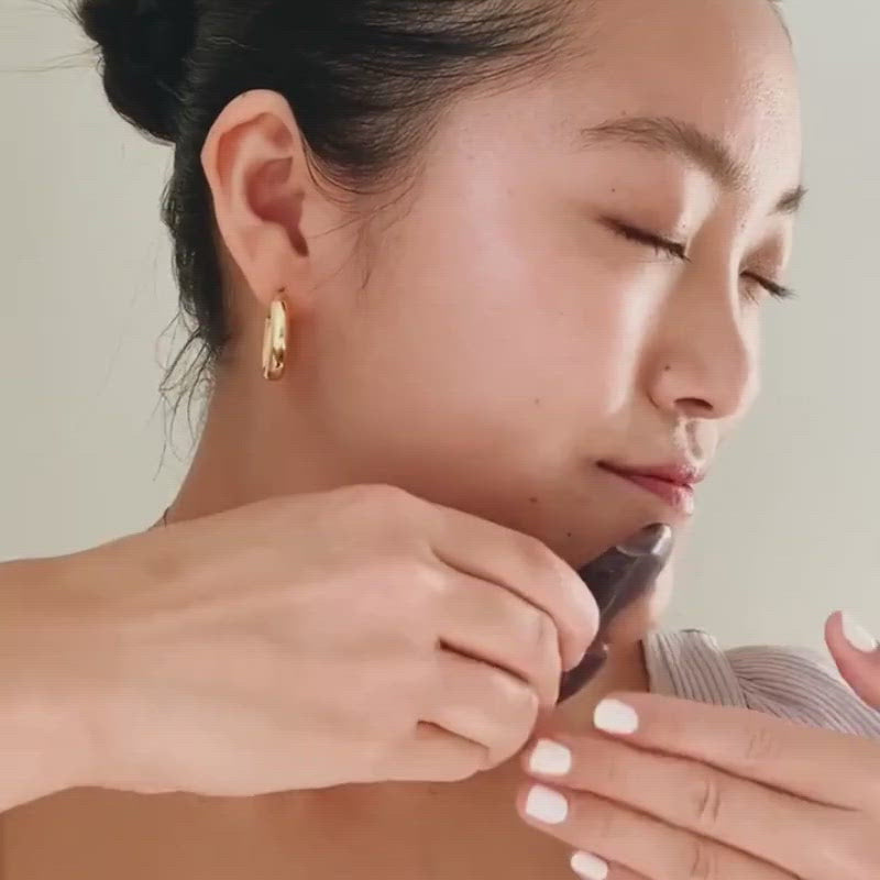 Woman using amethyst gua sha lifting tool along jawline